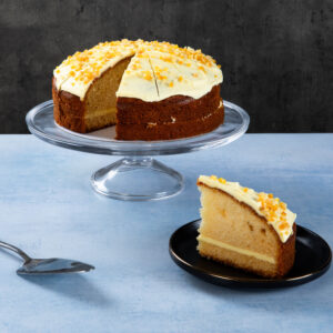 a round cake with white frosting and orange sprinkles with a slice on a plate