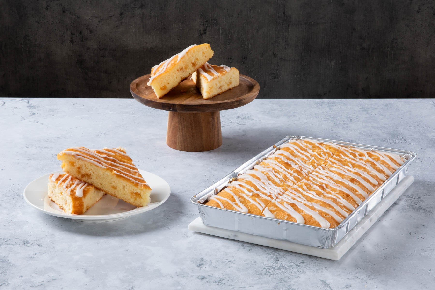 Lemon drizzle cake slices with white icing in a baking tray.