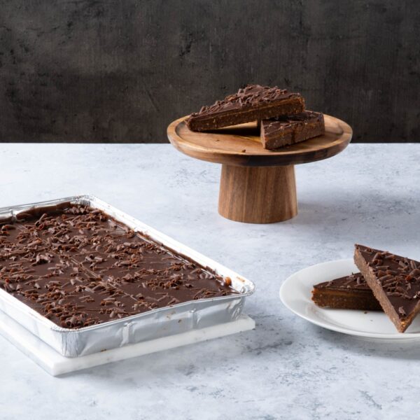 Chocolate cake with creamy frosting and chocolate topping on a wooden board.