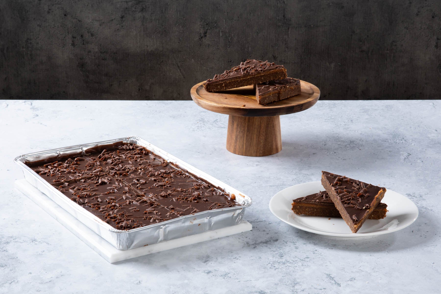 Chocolate cake with creamy frosting and chocolate topping on a wooden board.