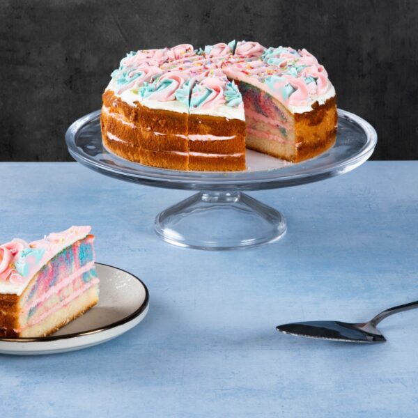 Rainbow cake with colourful layers and white frosting on a glass cake stand.