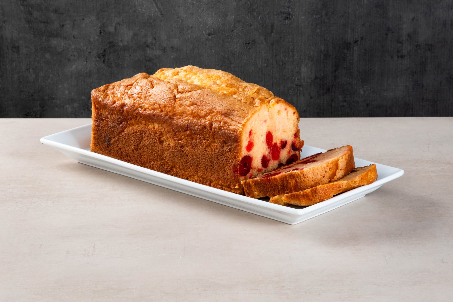 LHMC008-479.jpg Cherry loaf cake with sliced pieces on a white plate.