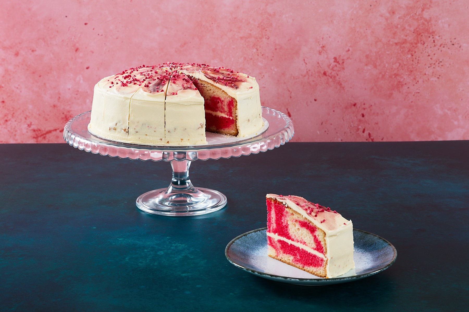 Raspberry Ripple Raspberry ripple cake with raspberry frosting and topping on a glass cake stand.